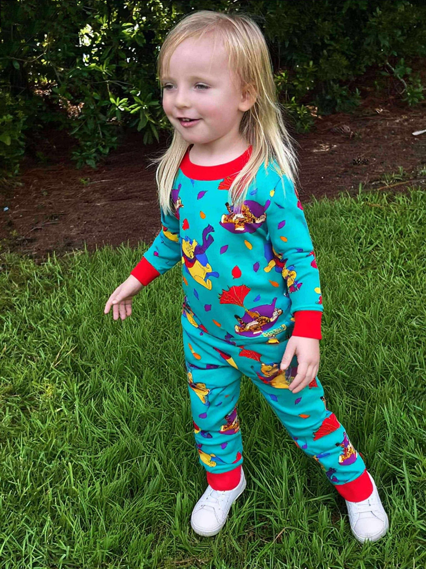 Child wearing colorful pajamas with a pattern of cartoon characters on grass.