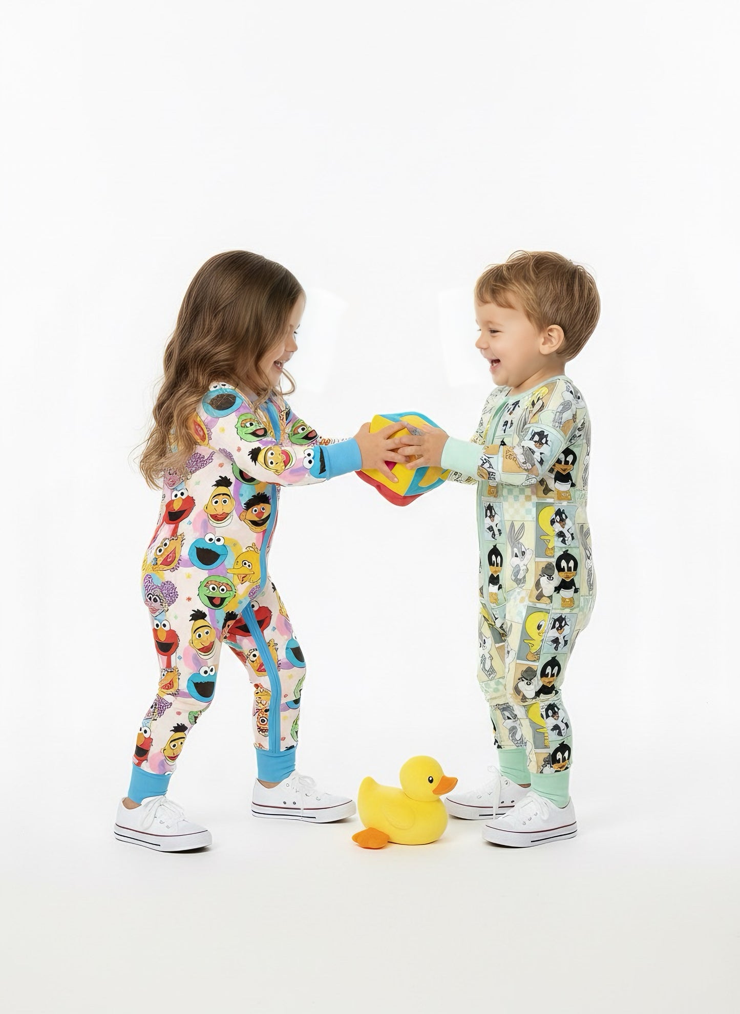 Two children wearing colorful pajamas with cartoon characters, holding a toy on a white background.