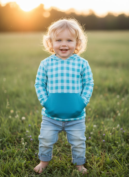 Child wearing a blue checkered hoodie and jeans standing in a grassy field with sunset in the background