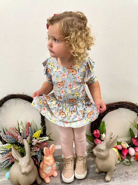 Child wearing Bunny Blooms Peplum Legging Set with floral and bunny design, surrounded by decorative rabbits and flowers.