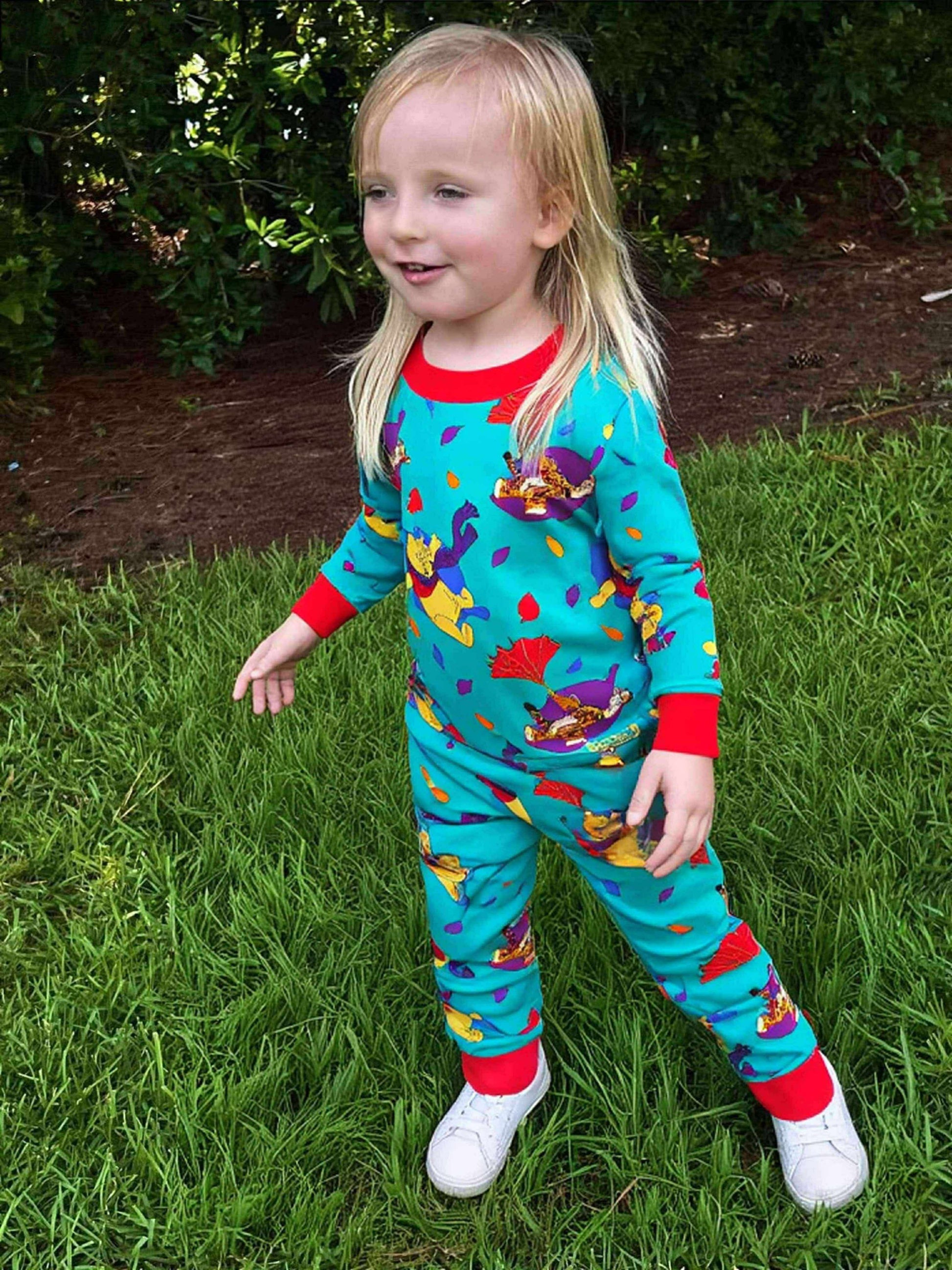 Child wearing colorful pajamas with a pattern of cartoon characters on grass.