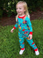 Child wearing colorful pajamas with a pattern of cartoon characters on grass.