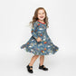 Child wearing a blue dress with a pattern of cars and animals on a white background
